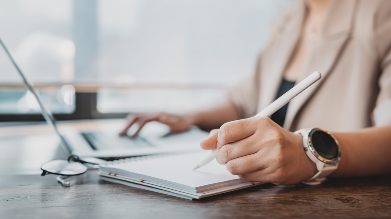 Woman works at laptop with pen and paper