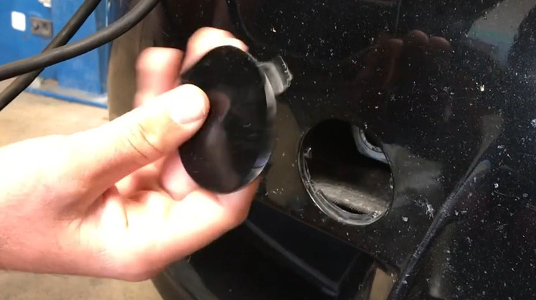 Hand holding tow hook cover in front of attachment point