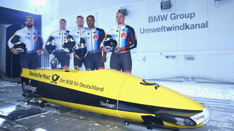 A BMW bobsled with a German bobsled team standing behind it.