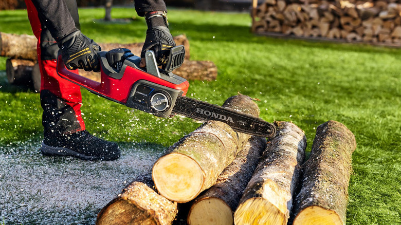 A person cutting logs with a Honda chainsaw.