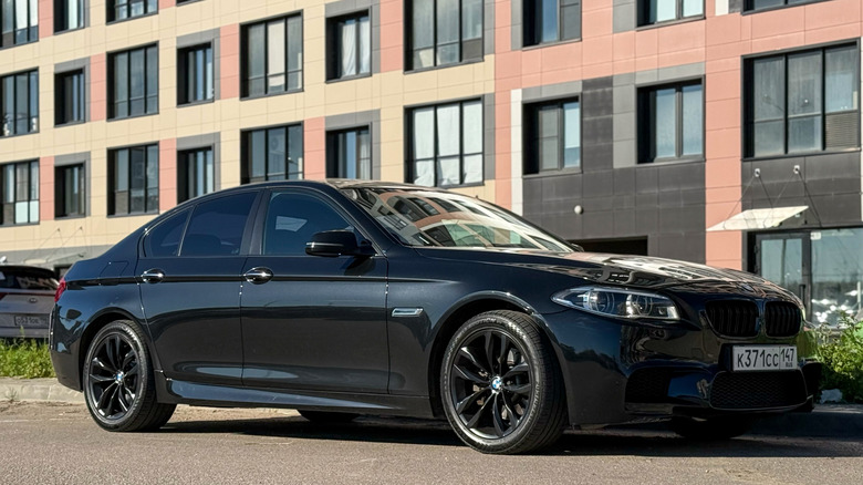 A black or Navy BMW M5 from the F10 generation parked at the side of a steet.