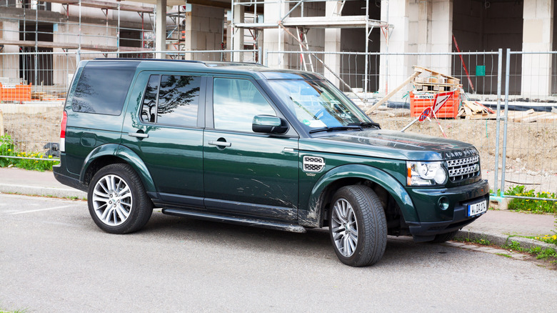 A green 2014 Land Rover Discovery parked outside a construction site.