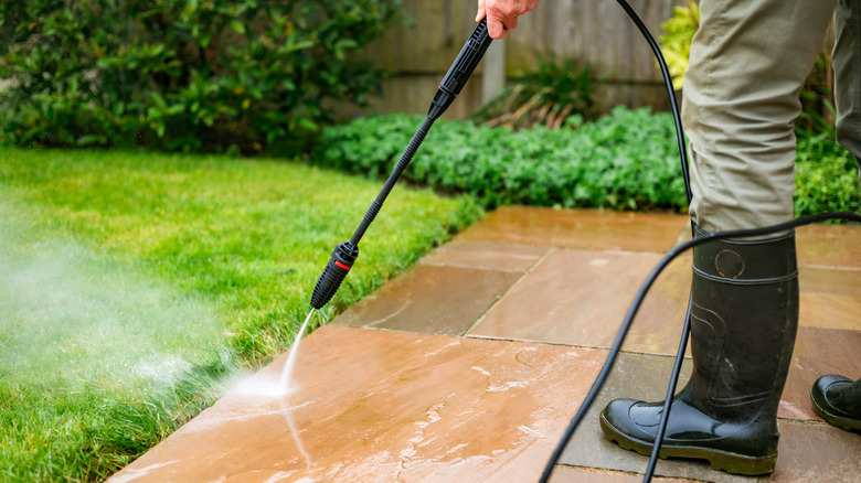 man using pressure washer to clean tile porch