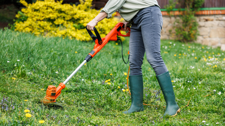 woman using string trimmer on grass lawn