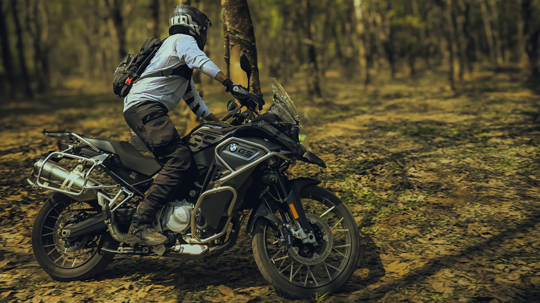 A fully kitted-out rider on a BMW F850GS adventure motorbike in the middle of a forest, riding the bike.