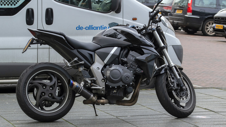 A black and gray Honda CB1000R motorbike parked next to an unidentified white vehicle in Amsterdam, The Netherlands.