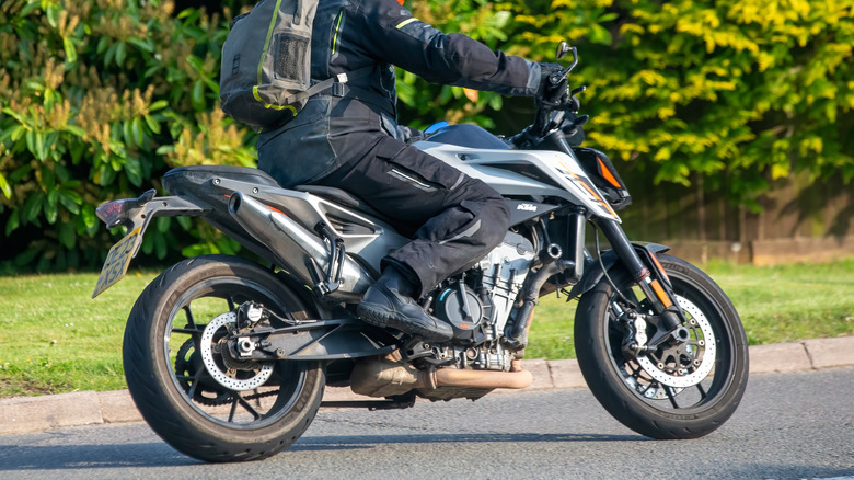A man in full riding gear and helmet riding a KTM 790 Duke L23 through the English countryside.