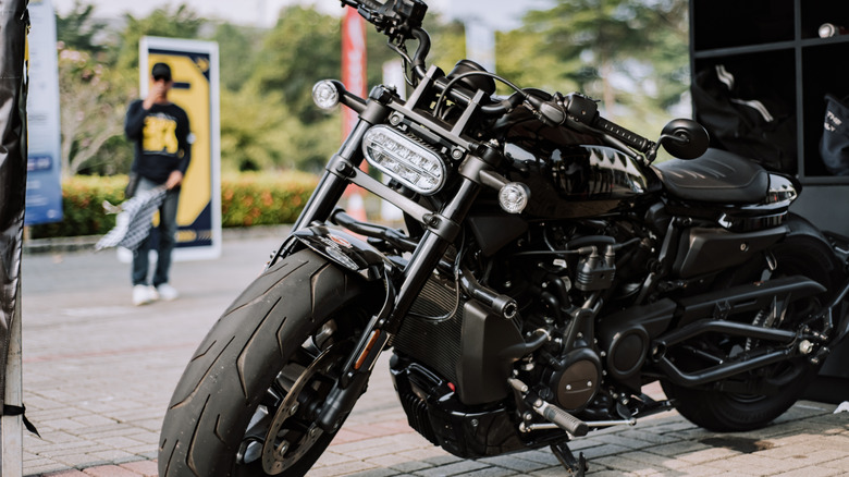 A black Harley-Davidson Sportster S parked on its kickstand outdoors, being showcased at a trade show.
