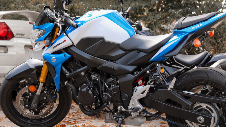 A white and blue Suzuki GSX-S750 naked bike parked outdoors with a silver car visible in the back.