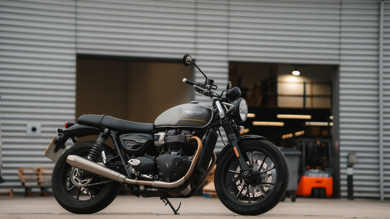 A retro gray Triumph Speed Twin motorcycle from 2024 parked outside a corrugated warehouse building in the UK.