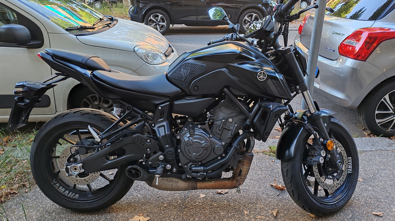 A black Yamaha MT-07 motorcycle parked on the sidewalk with other parked vehicles visible in the back.