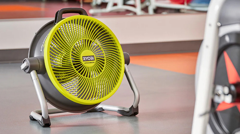 A 14-inch Ryobi fan on the floor blowing at fitness equipment.