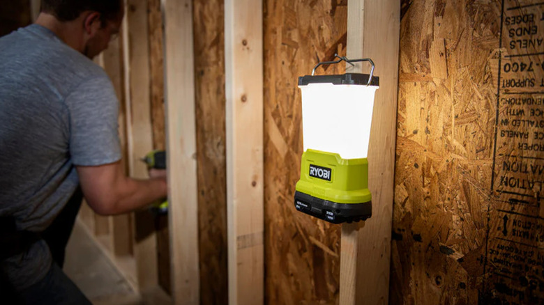 A Ryobi light hanging against an unfinished wall next to a worker.