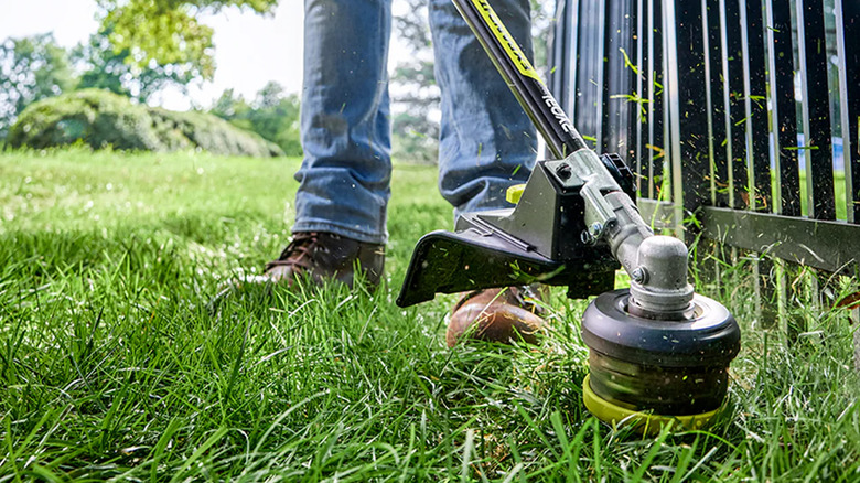 A person trimming along a fence line with a Ryobi string trimmer.
