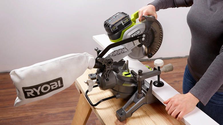 A woman cutting a piece of baseboard with a compound miter saw.