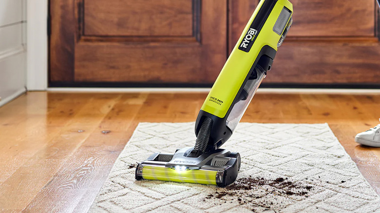 A person sweeping a floor with a Ryobi stick vacuum.
