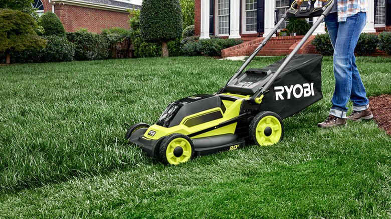 A person mowing a lawn with a Ryobi lawn mower.