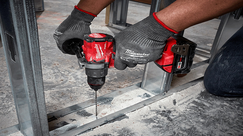 A worker using a hammer drill to drill into concrete and metal.