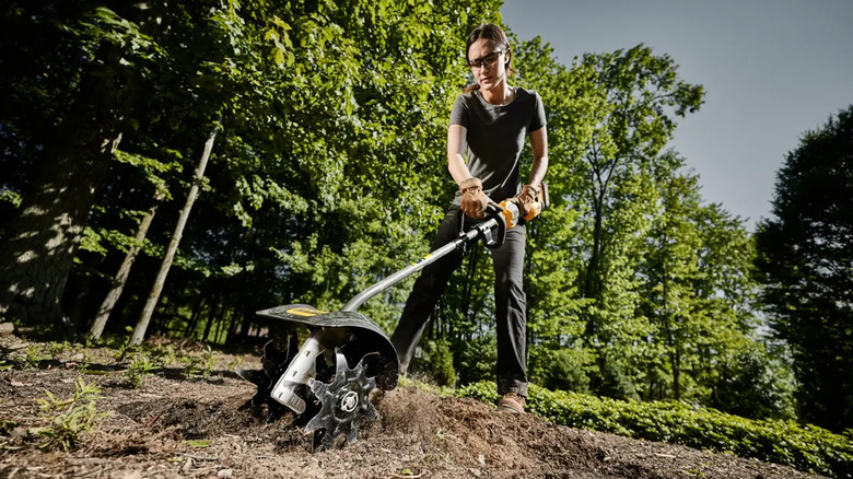 A woman using a DeWalt cultivator tool to dig a garden.