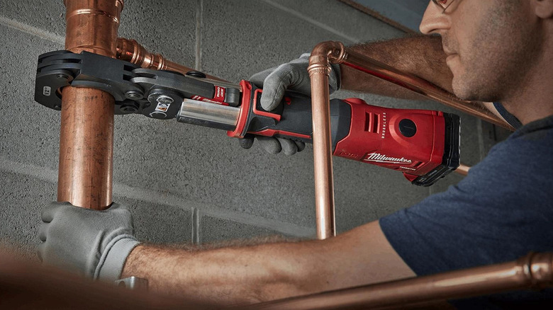 A plumber crimping a copper pipe with a Milwaukee press tool