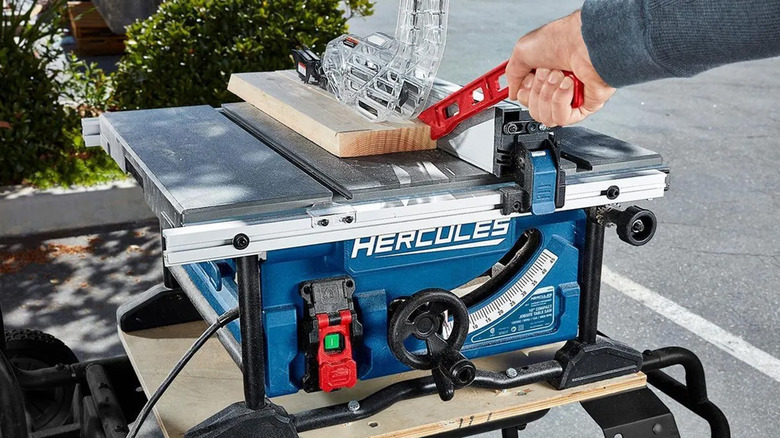 A man pushing a piece of wood through a table saw safely.