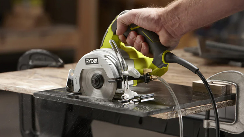 A man cutting a piece of dark-colored tile with a Ryobi tile saw.