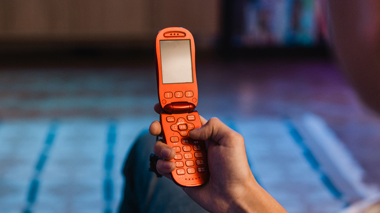 An orange flip phone being held in a dimly-lit room