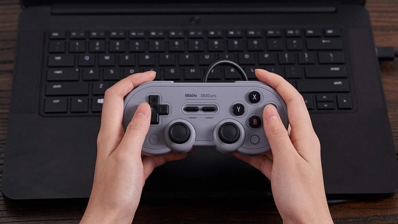 An 8BitDo controller with a '90s-inspired design being held in front of a laptop