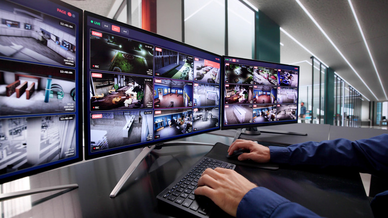 Three-monitor computer setup showing security camera footage with hands typing on a keyboard