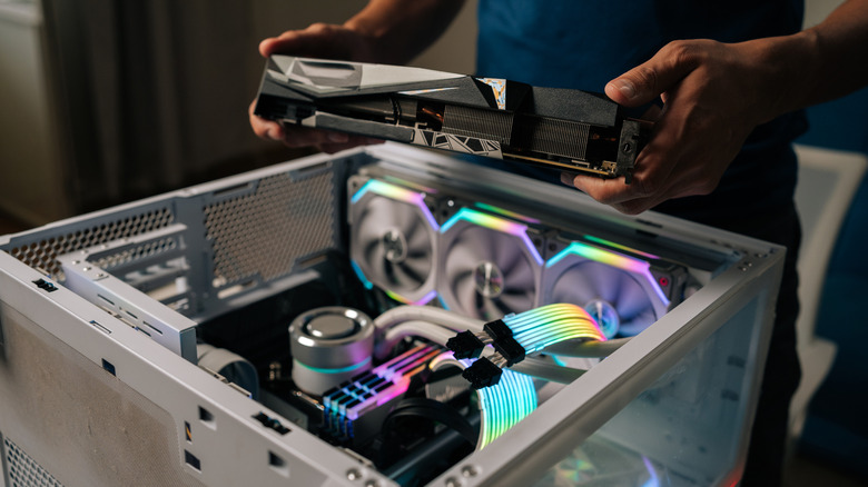 Two hands holding a computer part above an open PC case with multiple fans inside