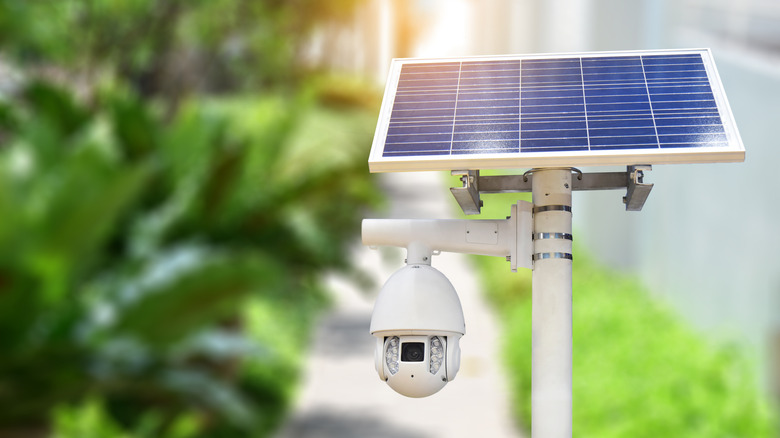 Solar panel with attached security camera against a blurred outdoor background