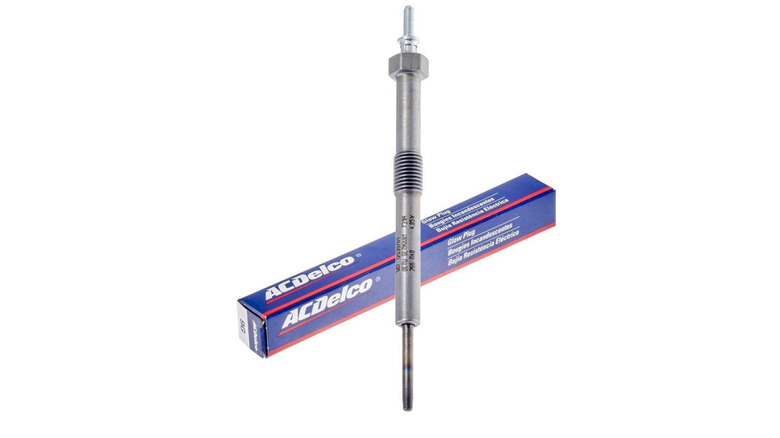 A metallic glow plug next to its box.