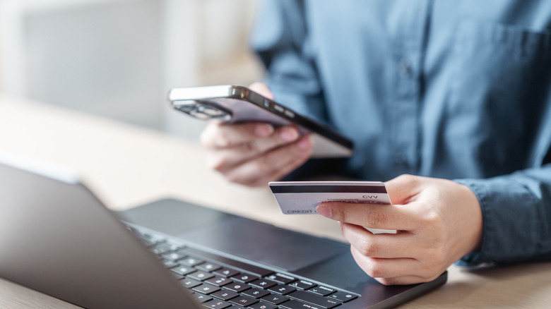 A person on their phone and computer holding a credit card and making a purchase