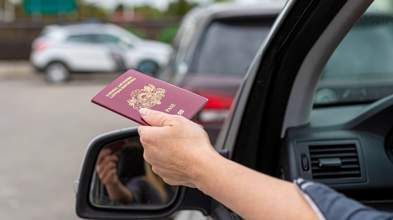 a person handing their passport out the window of a car