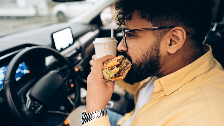 a person eating a burger in the driver seat of a car