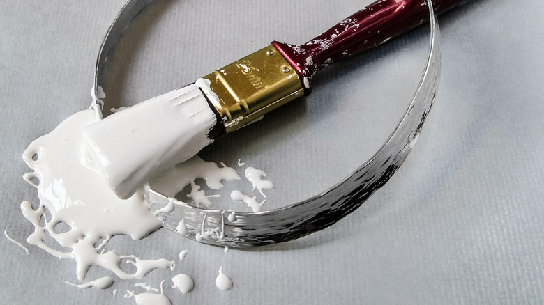 A wet paint brush with white paint on a metal ring