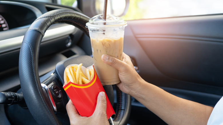 A lady holding snacks infront of a steering wheel