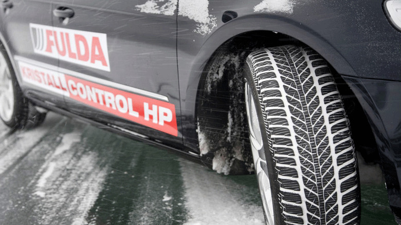 Close-up of a black car with Fulda Kristall Control HP winter tires driving on a snow-covered road.