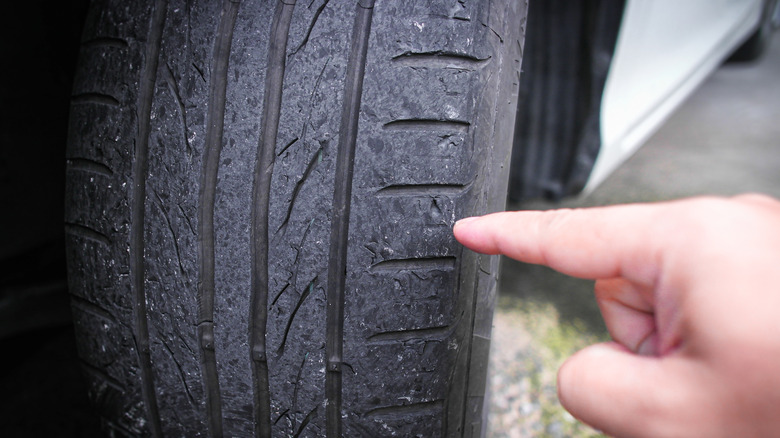 A hand pointing the index finger at tires that have clearly been worn down to the point of being bald.