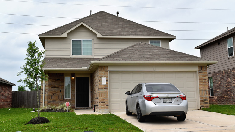A suburban home with an economical silver car parked in the driveway of the beige house.