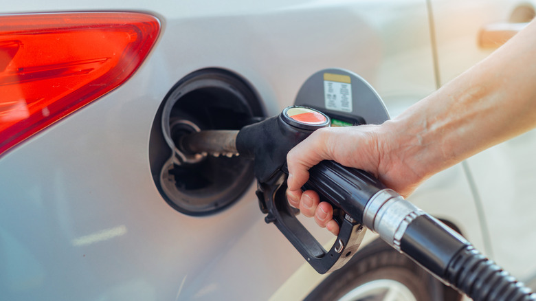 A person refueling a silver car at a gas station, with the nozzle in the gas tank.