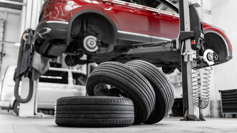 A red car mounted on a lift, with tires stacked on each other in the foreground inside a garage.