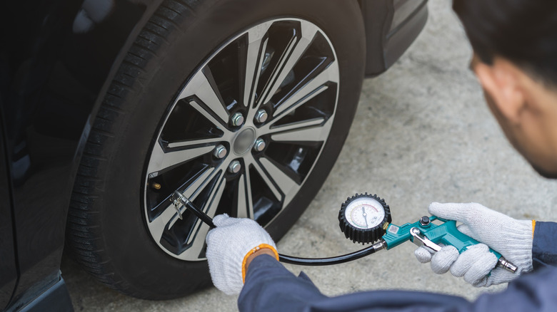 An auto mechanic in overalls testing the PSI in a car tire using a blue handheld gauge.