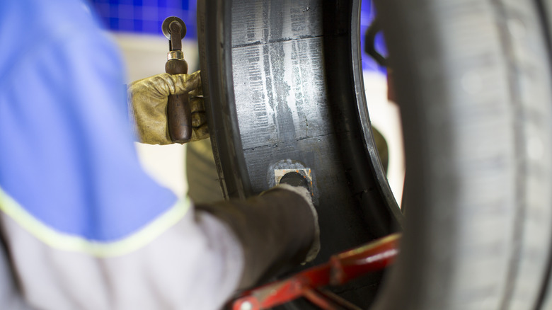 A mechanic in full kit patching the inside of a damaged car tire in a garage.