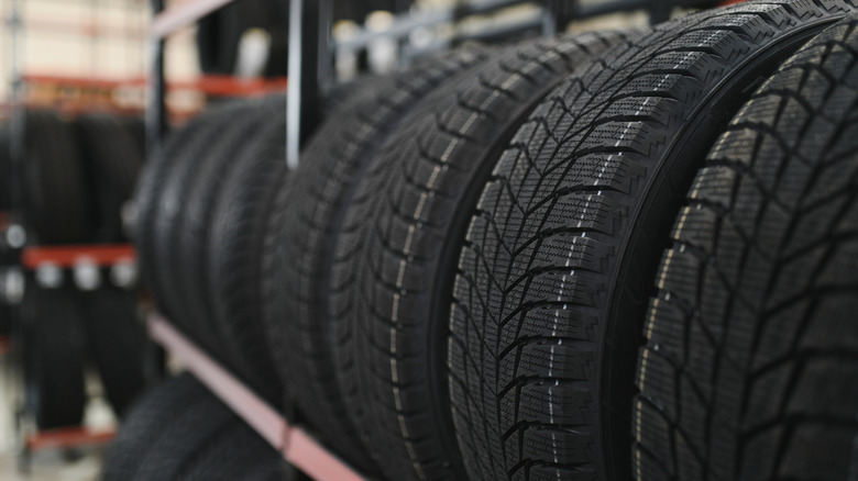 A line of new tires placed in a line on a storage rack that is red in color in a warehouse.