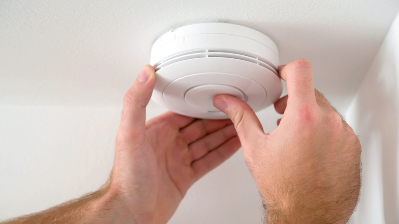 A person installing a smoke detector on their ceiling
