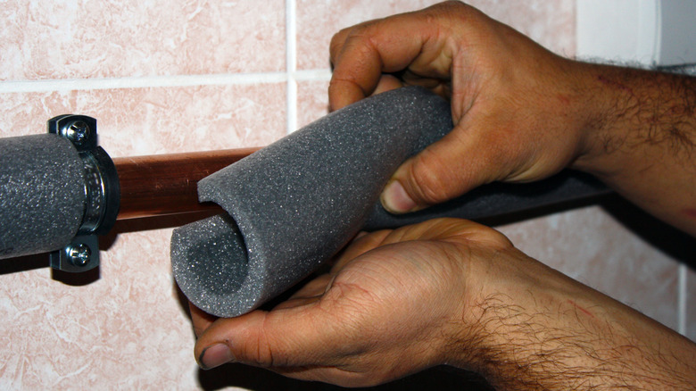 A person fitting foam over pipes as insulation