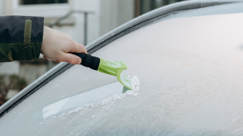 A person removing ice from a windshield with an ice scraper