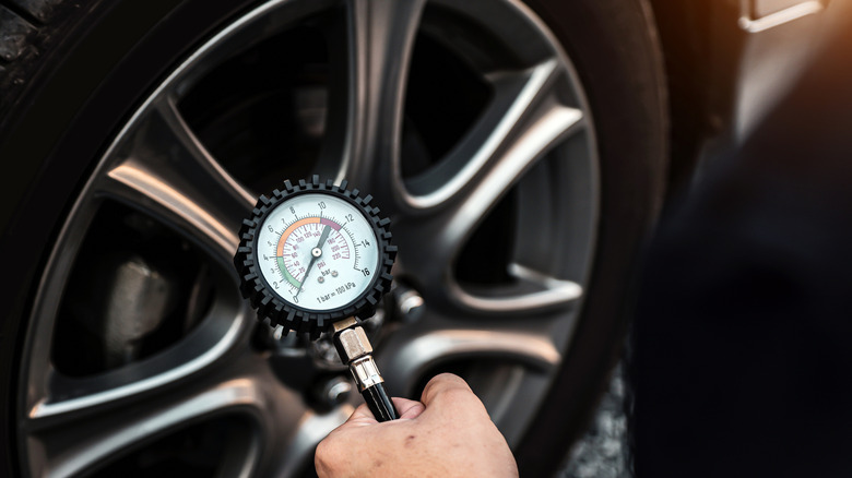 A person measuring their car's tire pressure with a gauge