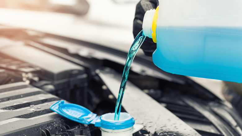 A person pouring windshield washer fluid into the engine